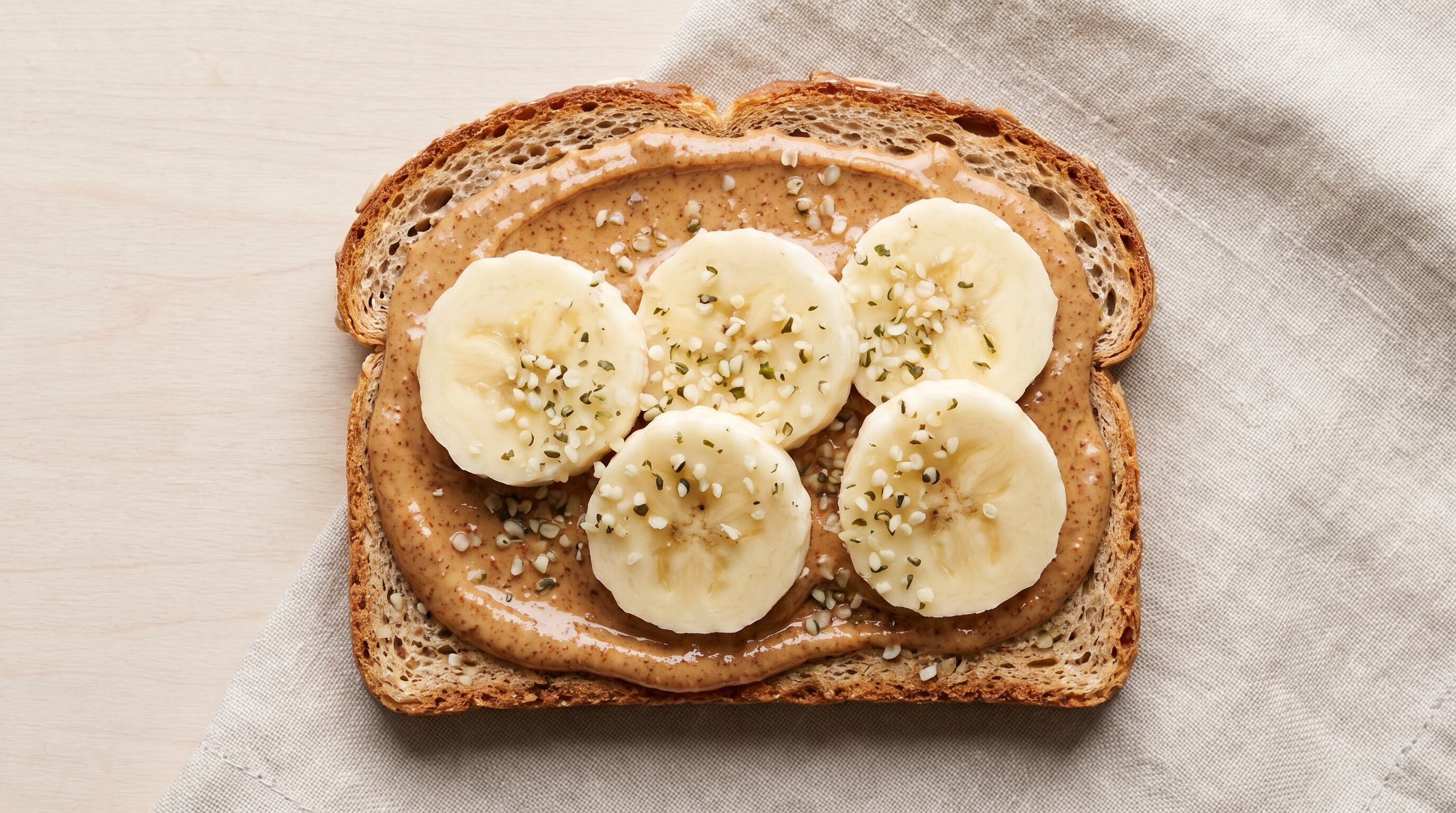 Pan de granos germinados con mantequilla de almendra, semillas de cáñamo y banana prioriza granos menos refinados y concentra semillas, frutos secos y fruta en una sola preparación. (Imagen Ilustrativa Infobae)