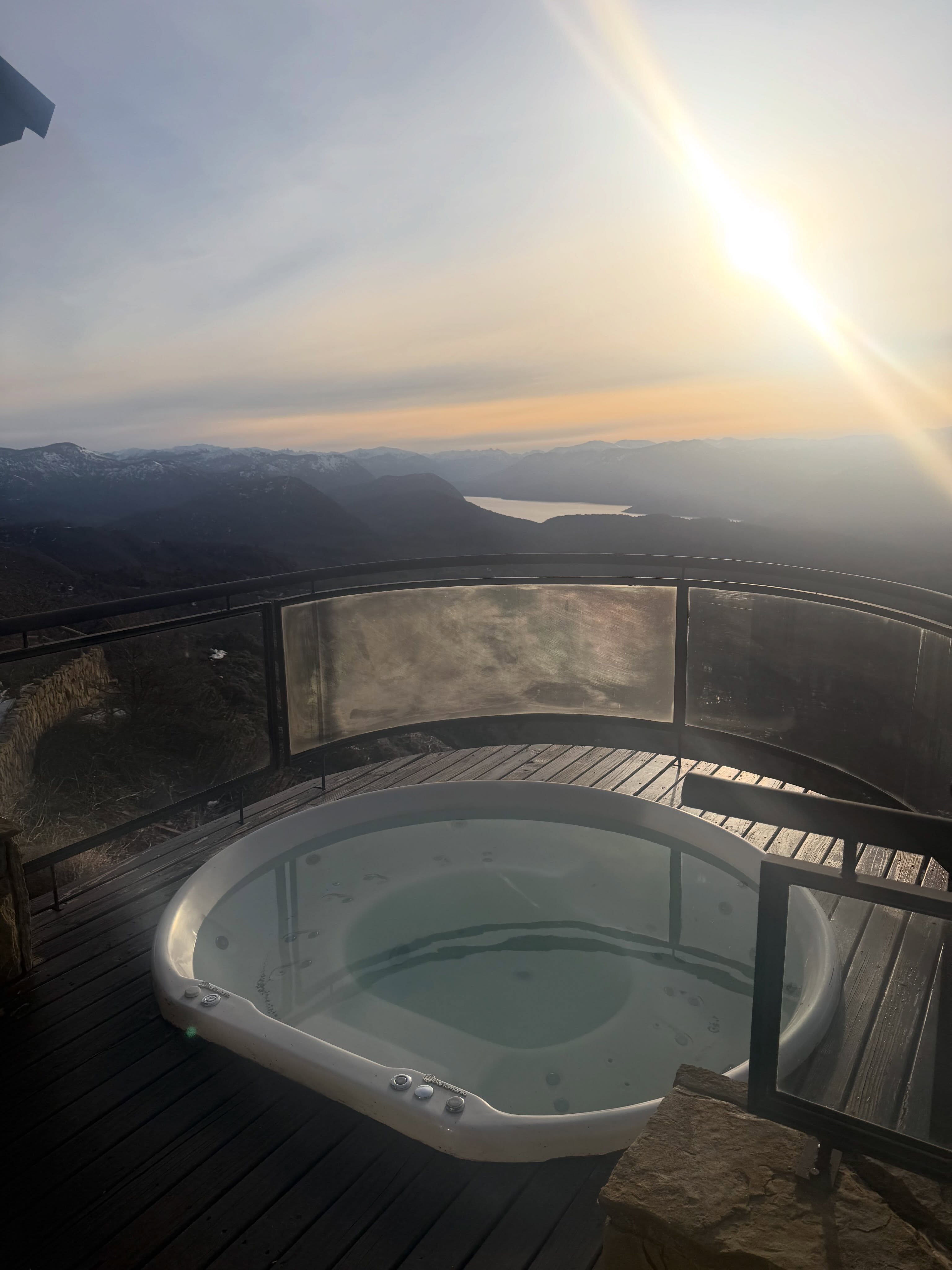 Un hidromasaje sobre un deck de madera ofrece una vista hacia las montañas y un lago