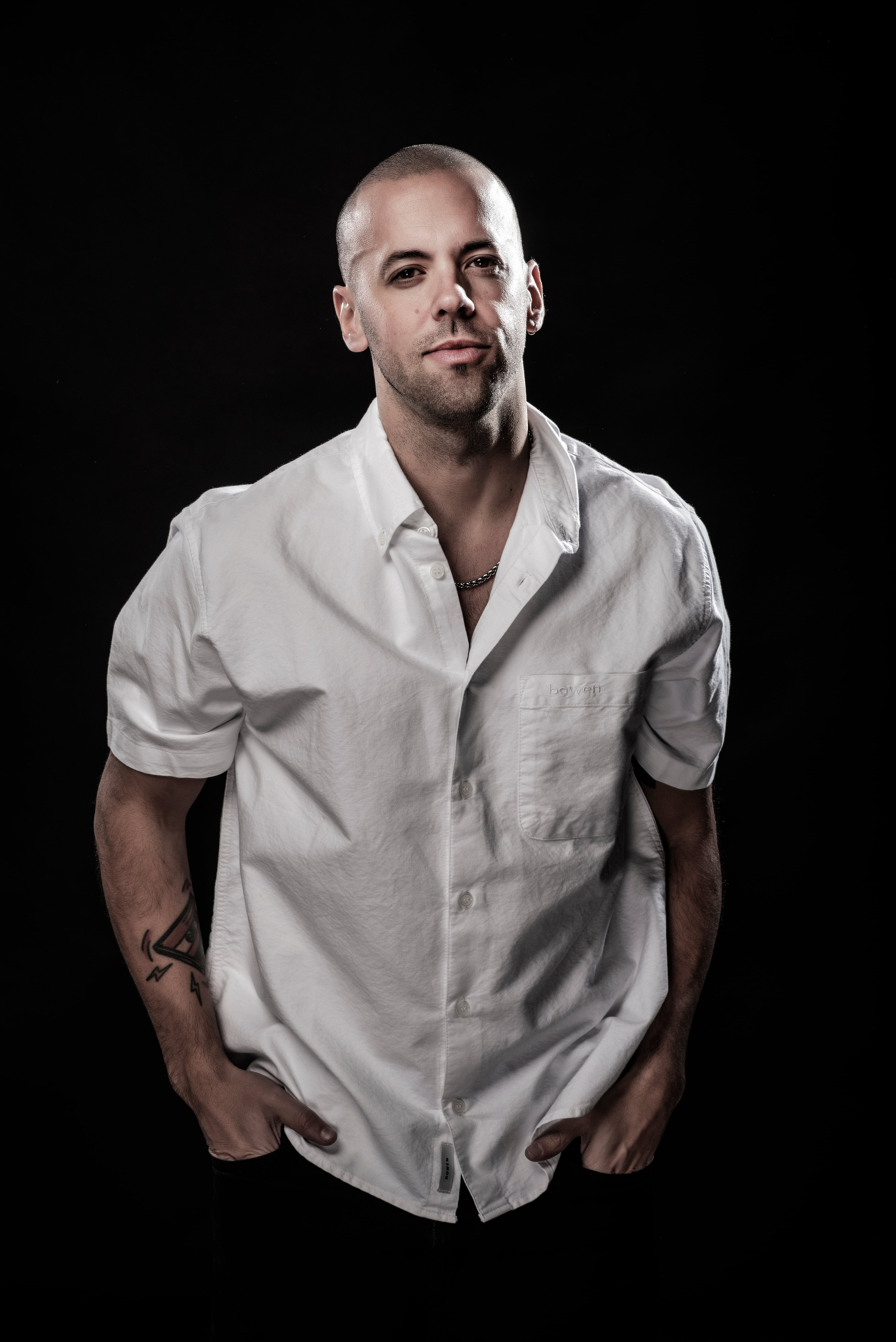 Mati Napp posa en un estudio, con una camisa blanca desabrochada, las manos en los bolsillos y un collar de plata visible.