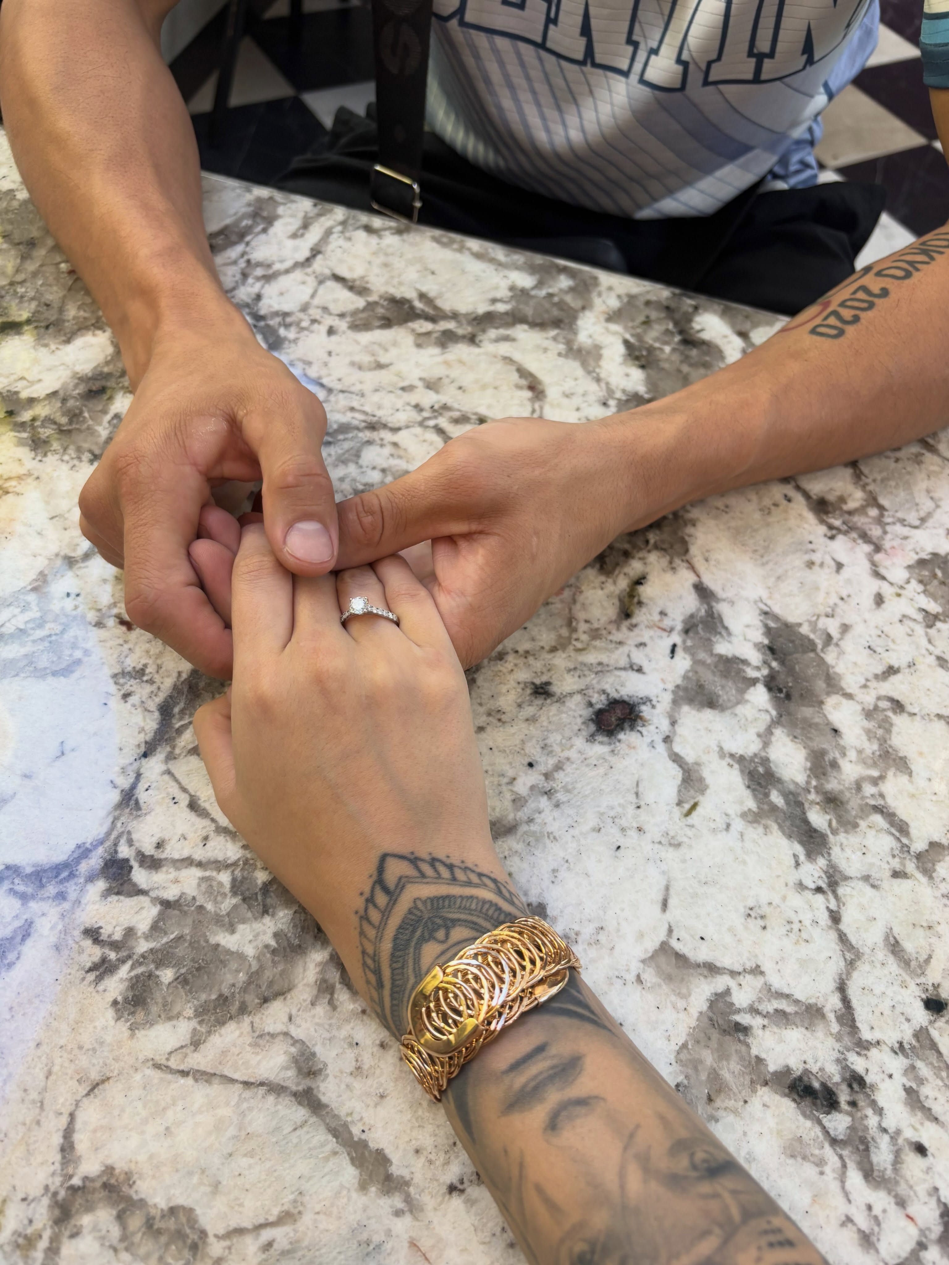 Unas manos entrelazadas sobre una mesa de mármol sostienen un anillo de compromiso con un diamante en el dedo anular de Chuly, la flamente futura esposa del Bebu Verón