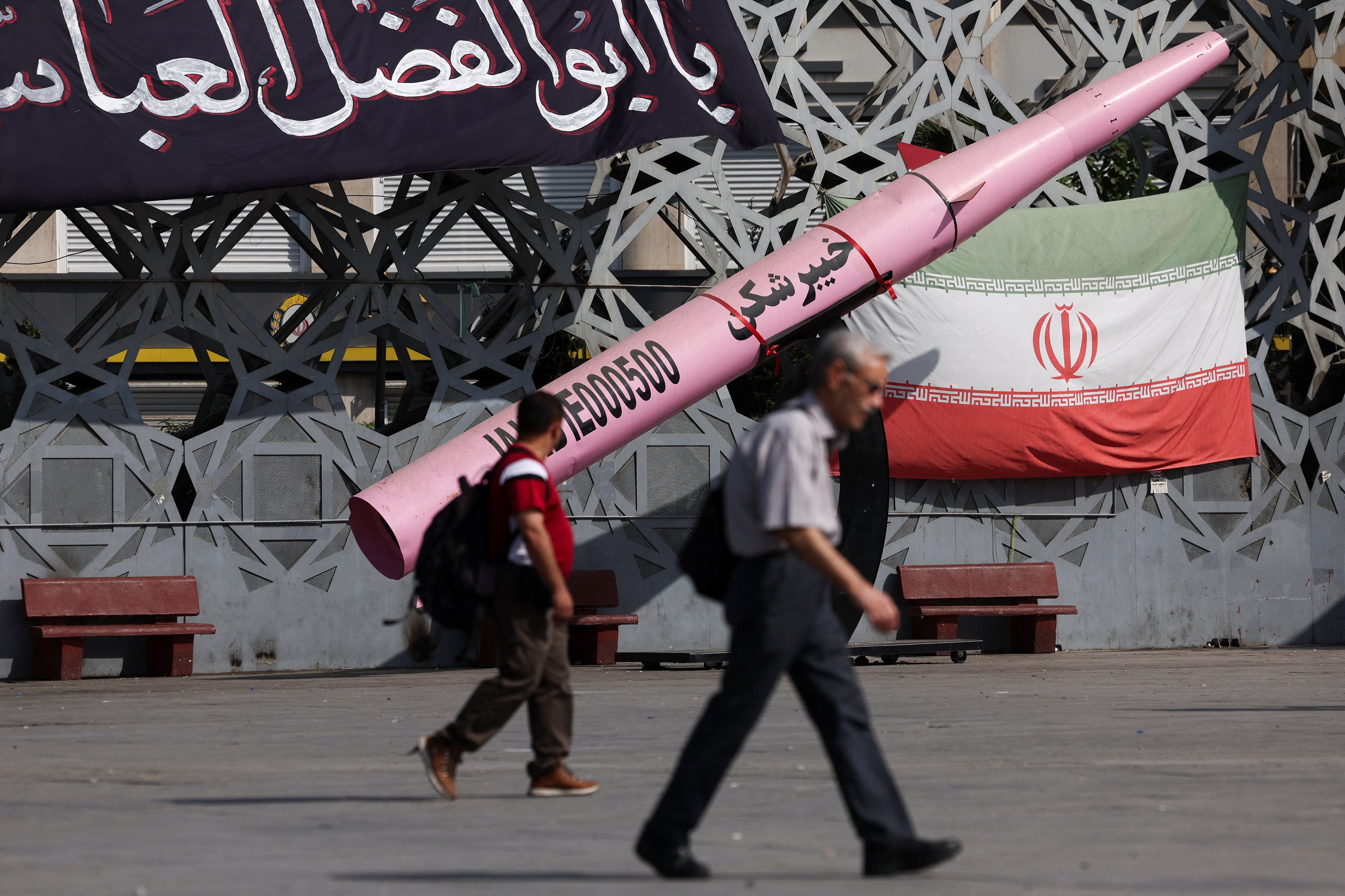 Varias personas caminan junto a una réplica simbólica de un misil iraní y una bandera iraní en la plaza Imam Hussein de Teherán (Majid Asgaripour/WANA vía REUTERS)