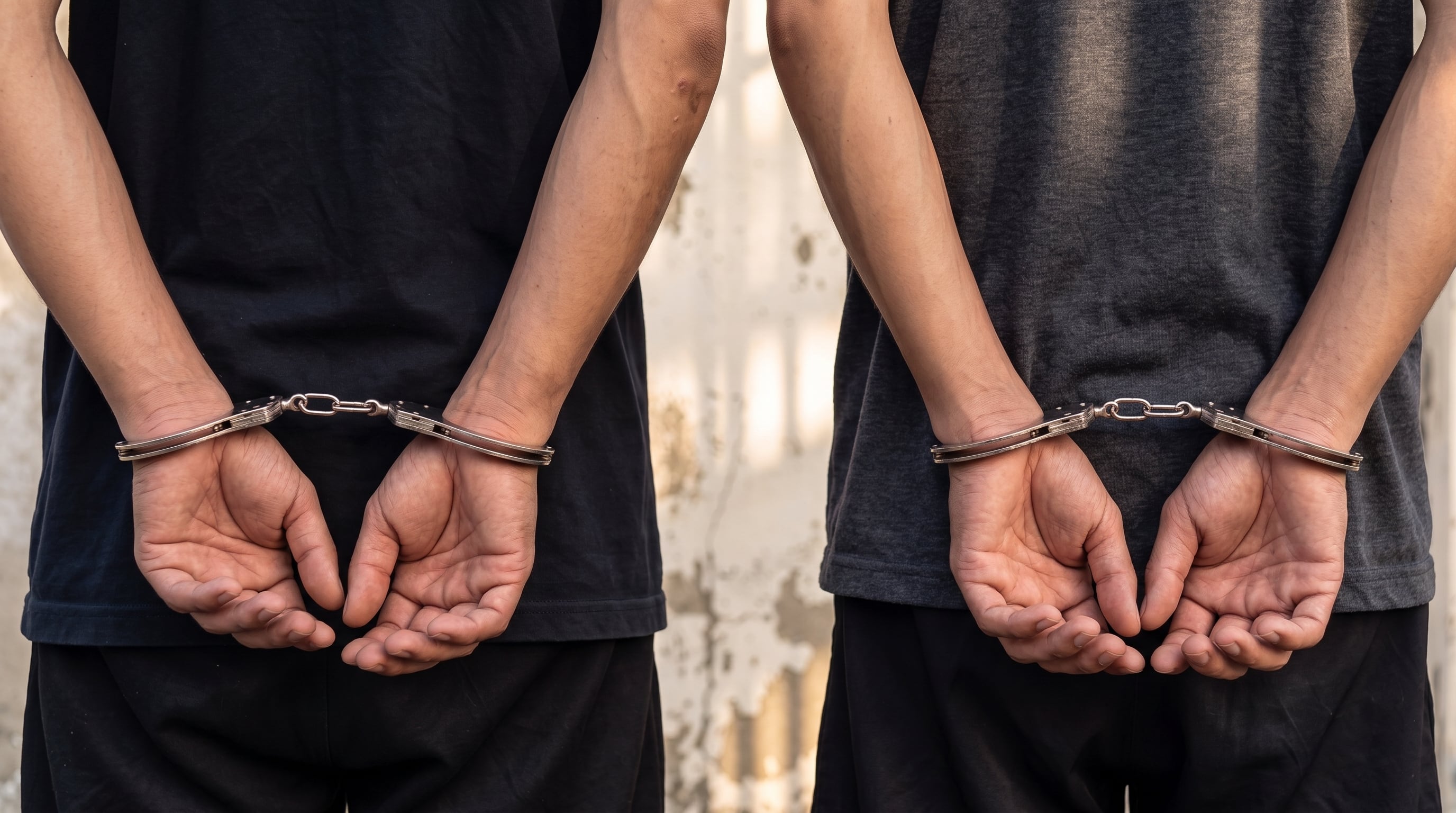 Dos individuos permanecen de pie con las manos sujetas con esposas metálicas por la espalda. (Imagen Ilustrativa Infobae)
