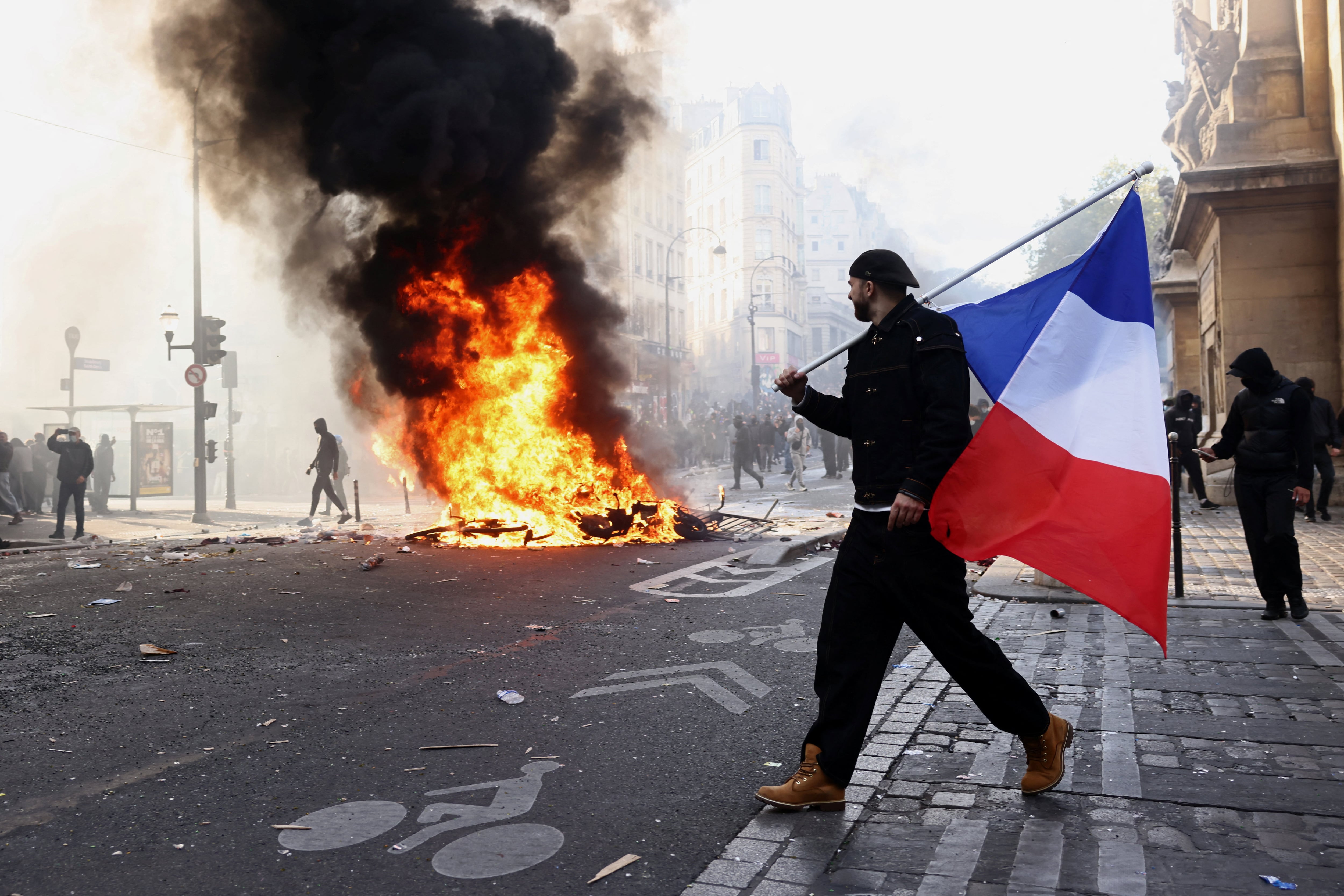 Un manifestante sostiene una bandera francesa junto a objetos en llamas en medio de enfrentamientos en una calle cercana a la plaza de la República, París, Francia, el 17 de octubre (REUTERS/Jack Taylor)