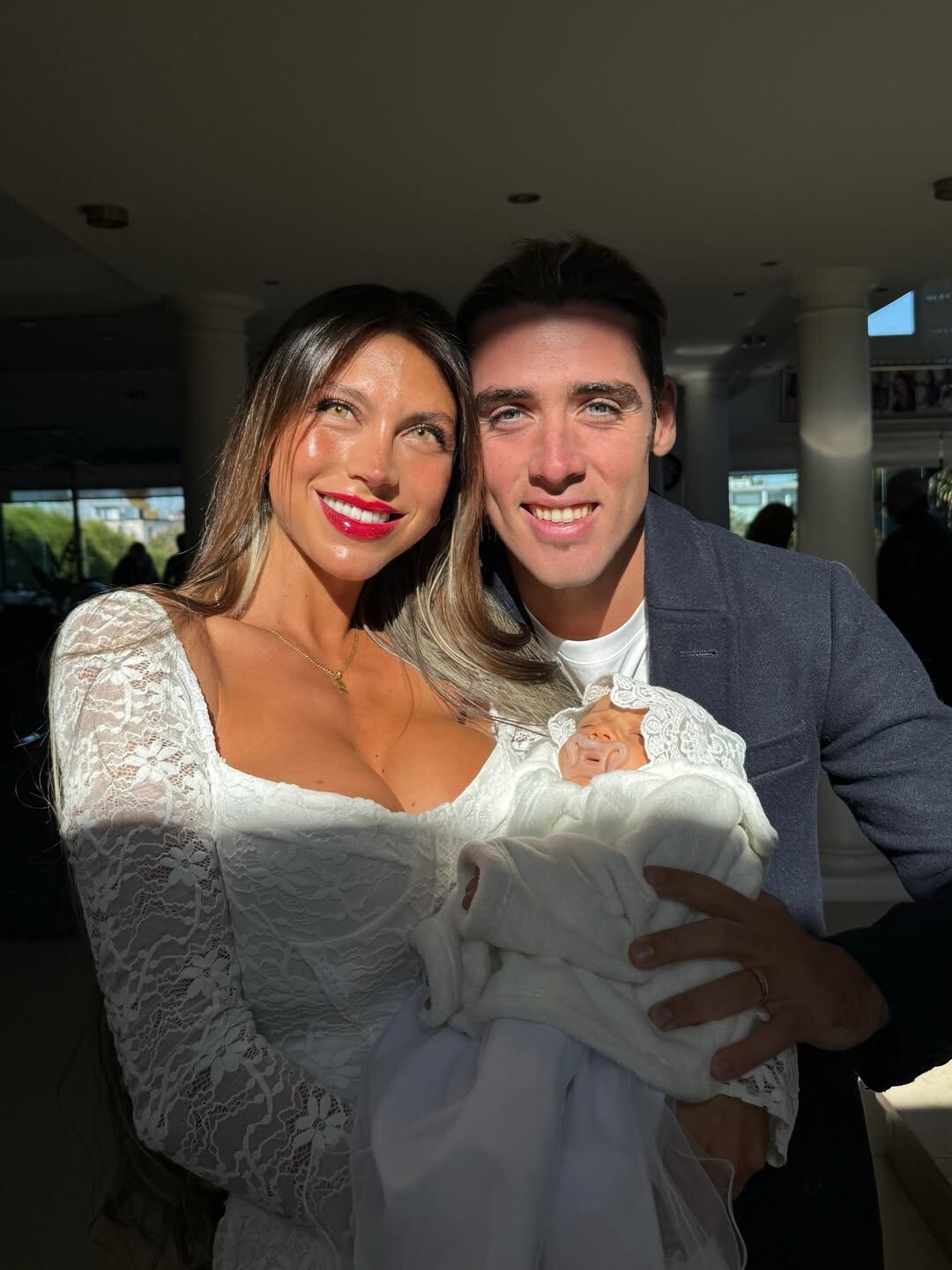 Cielo López y Claudio Spinelli posan sonrientes mientras él sostiene a su bebé envuelto en una manta blanca.