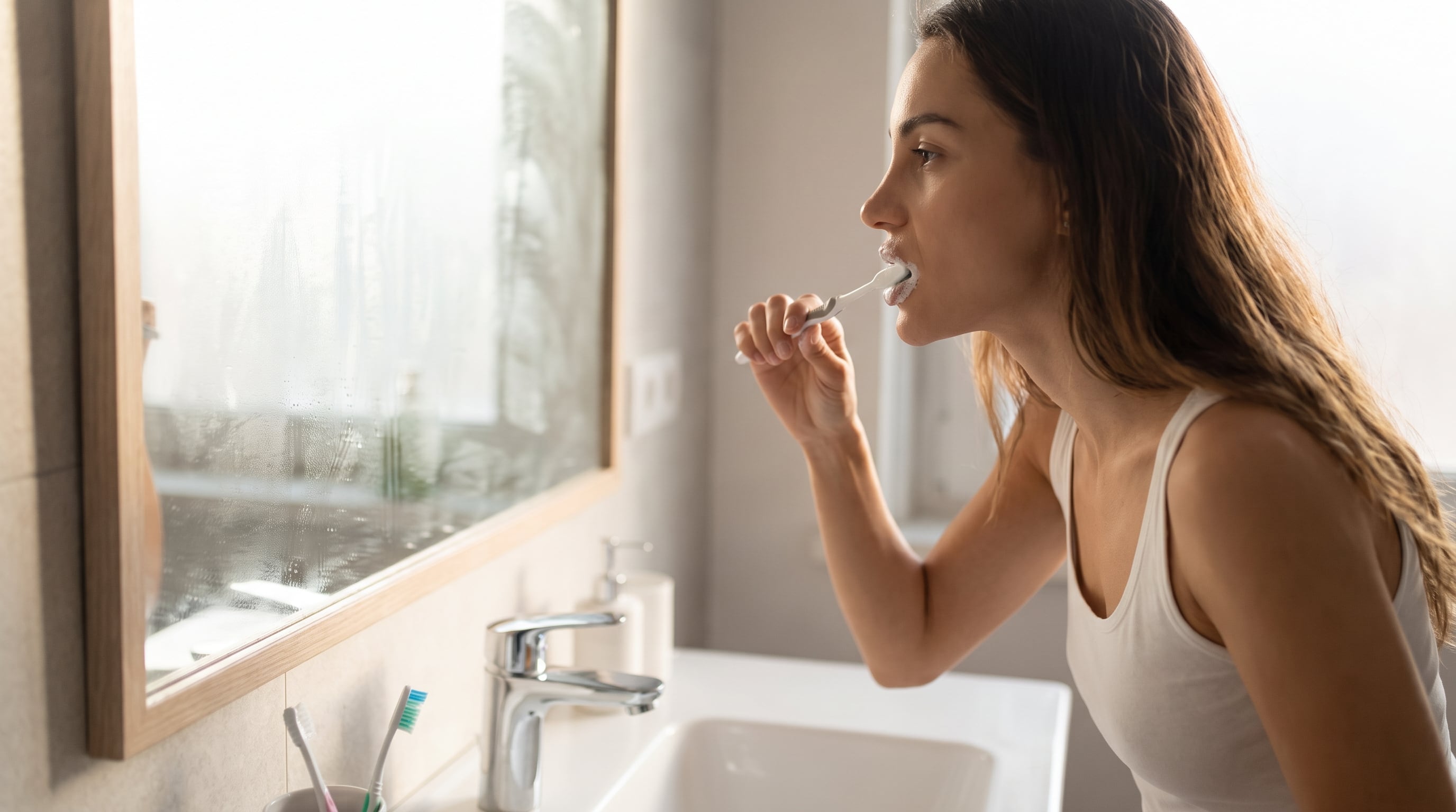 Una mujer se cepilla los dientes frente al espejo de un cuarto de baño durante su rutina diaria de higiene personal. (Imagen Ilustrativa Infobae)