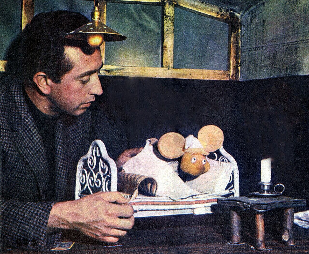 El actor Peppino Mazzullo observa a la marioneta del ratón Topo Gigio recostada en una cama en miniatura.