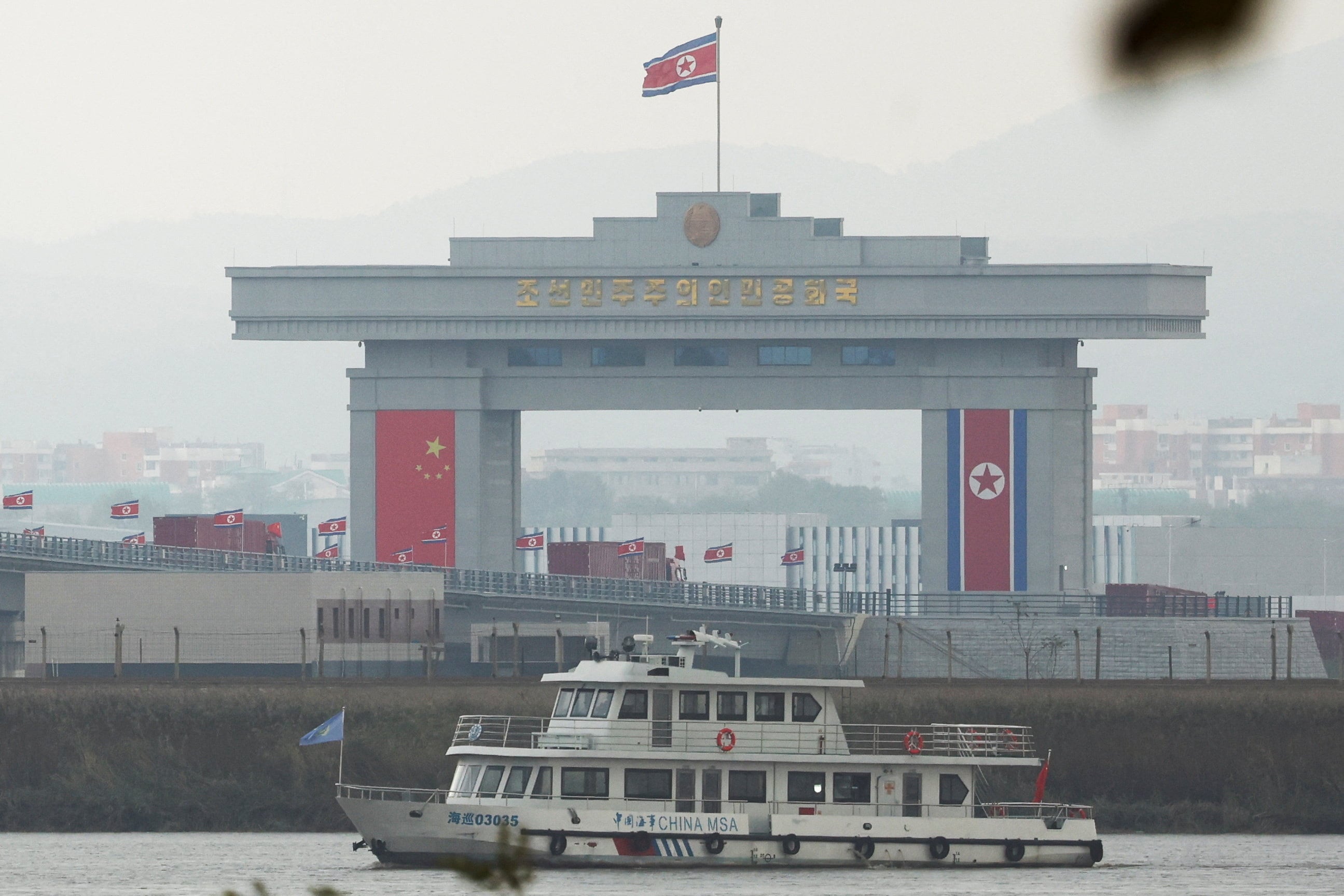 Un buque patrullero marítimo chino navega por el río Yalu mientras camiones adornados con banderas chinas cruzan el recién inaugurado Puente del Nuevo Río Yalu hacia Sinuiju, Corea del Norte, desde la Nueva Zona de Dandong, China, vista desde Dandong, provincia de Liaoning, China, el 15 de octubre de 2026 (REUTERS/Florence Lo)